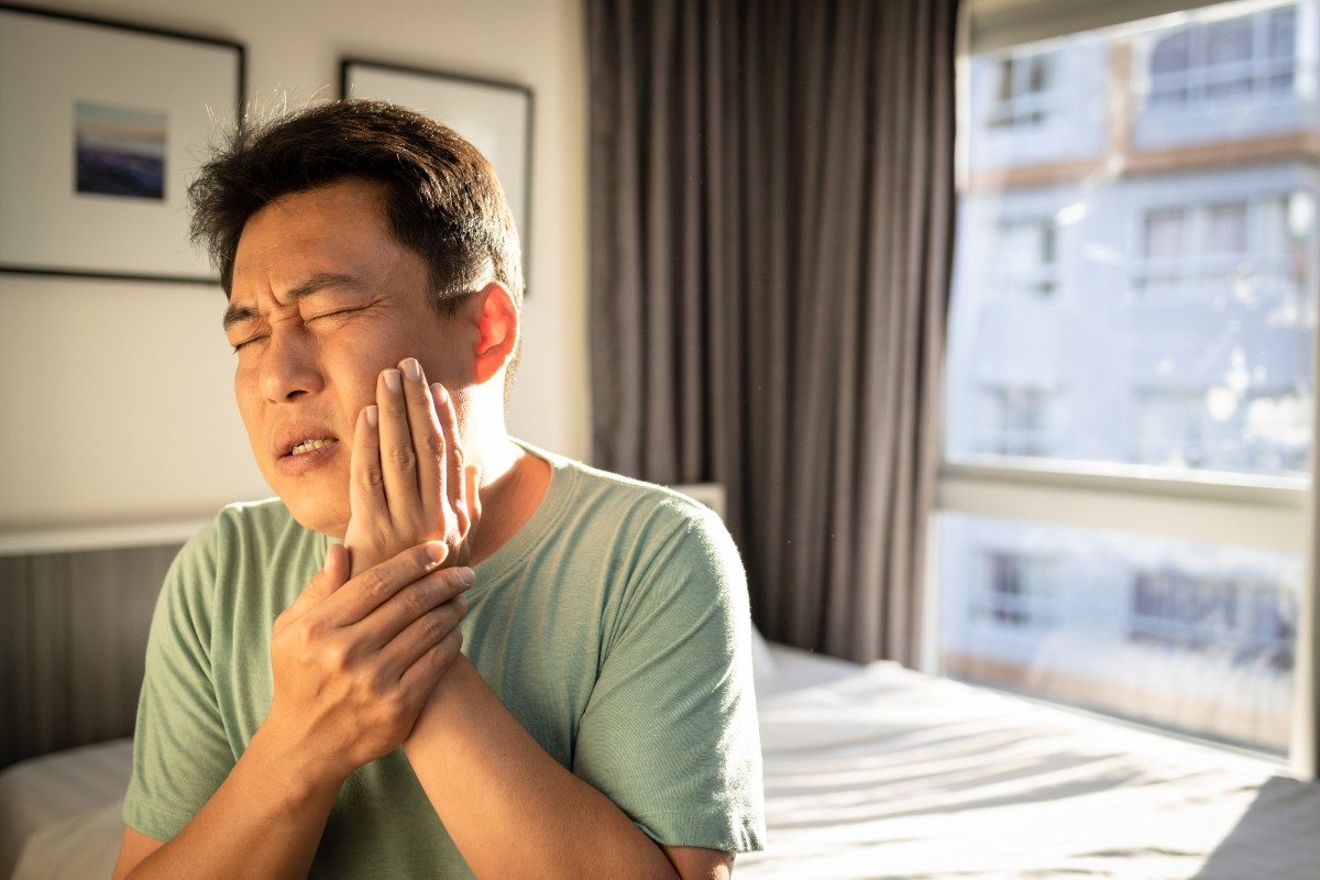 インプラント治療後に腫れた頬をおさえて痛がる男性